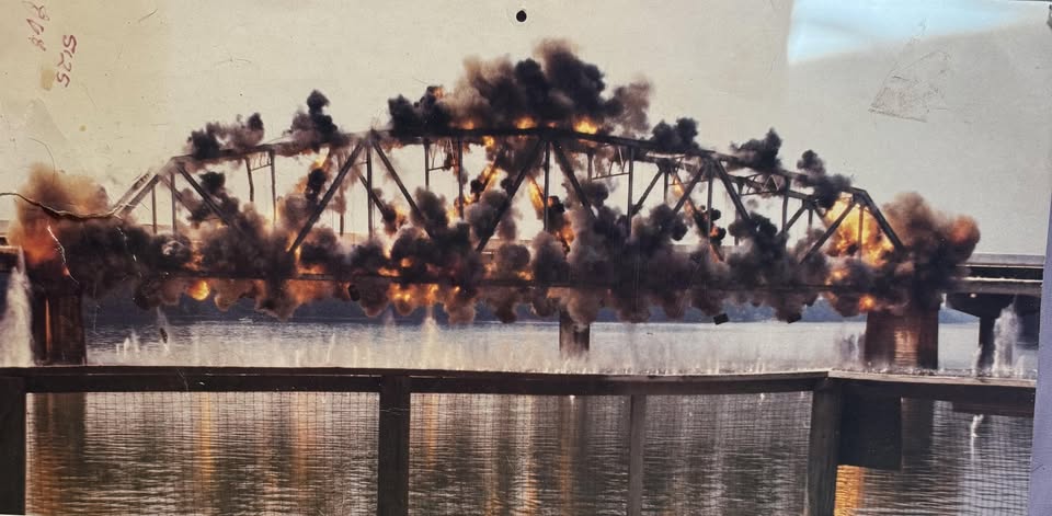 Controlled demolition blast bringing down a steel truss bridge over a river